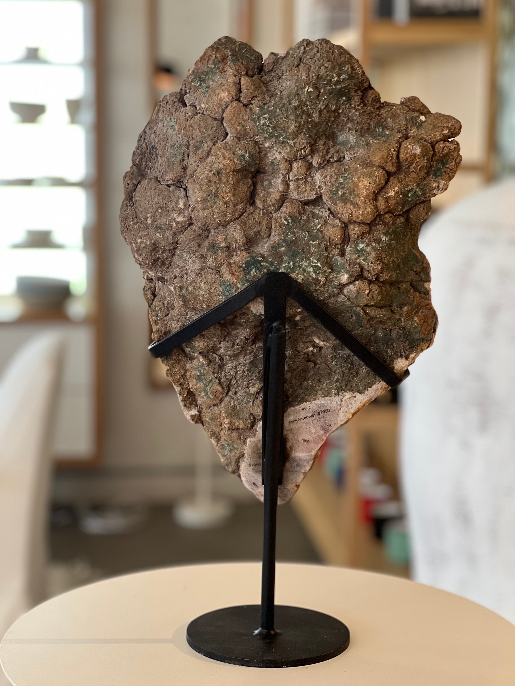 rear view of the pink amethyst stone on its black metal stand with blurred background
