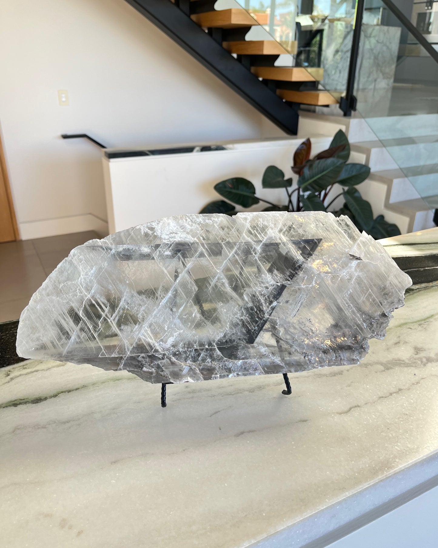Decorative selenite sculpture on a stand in a modern indoor setting with stairs and plants.
