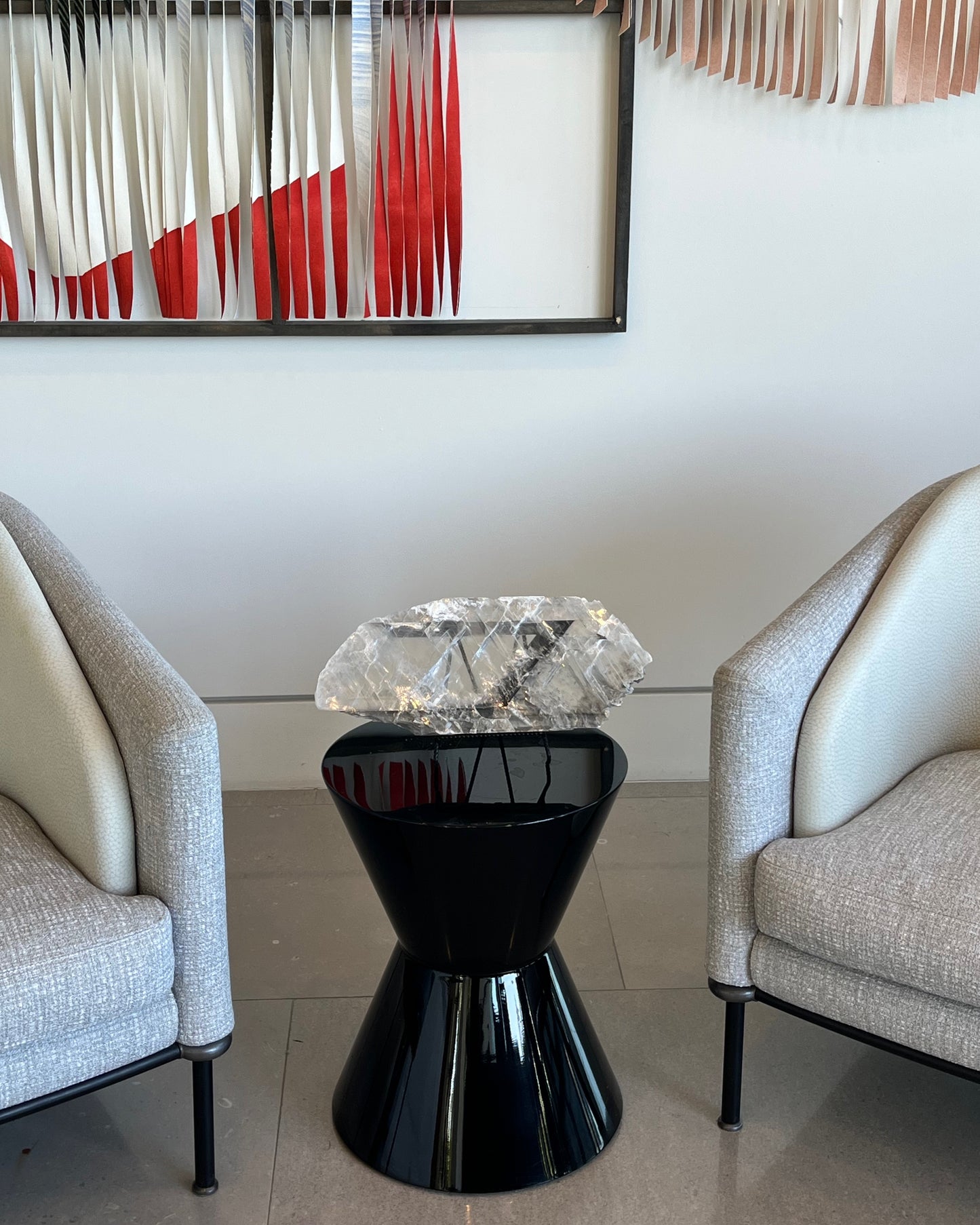 Modern black side table with crystal top between two gray chairs, abstract art in the background.