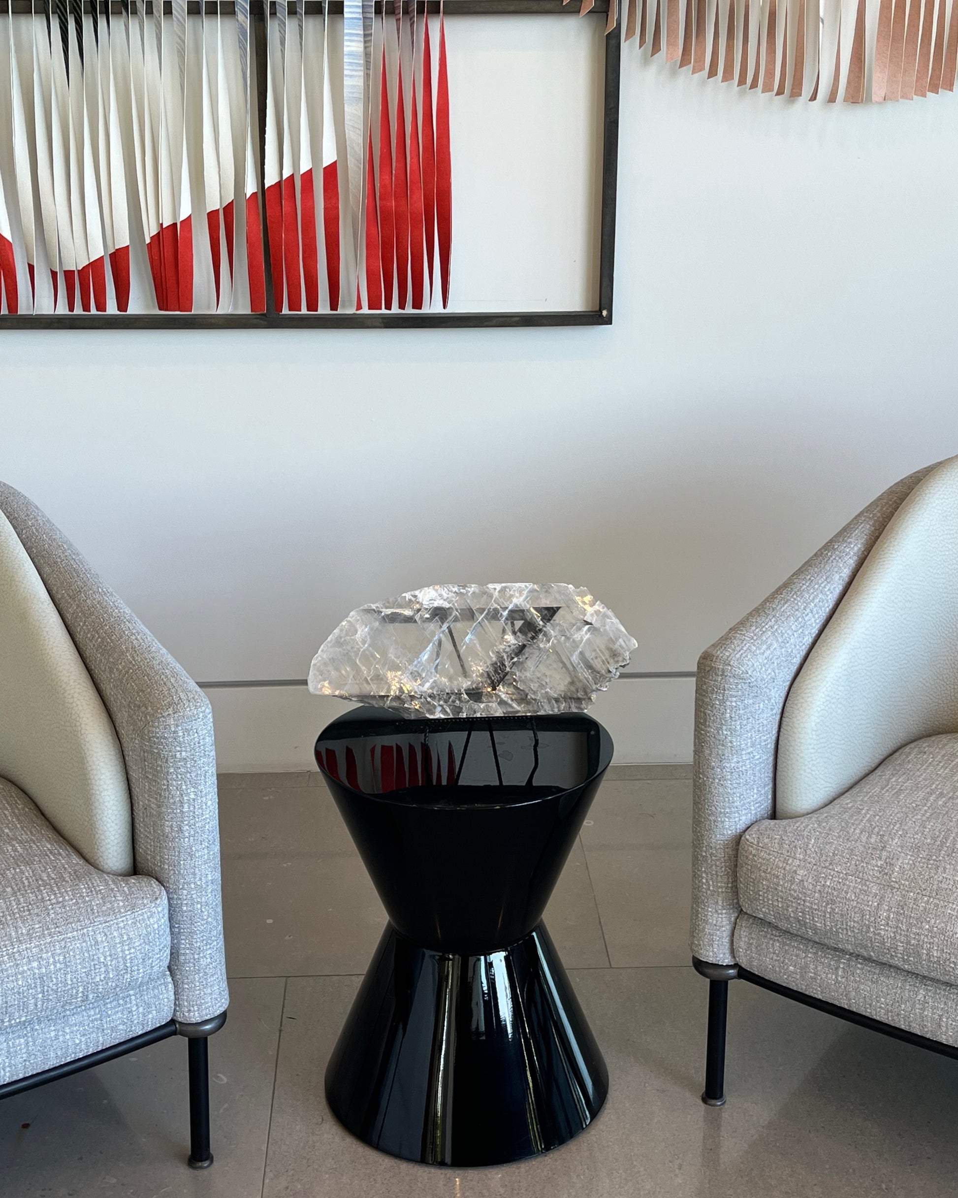 Modern black side table with crystal top between two gray chairs, abstract art in the background.