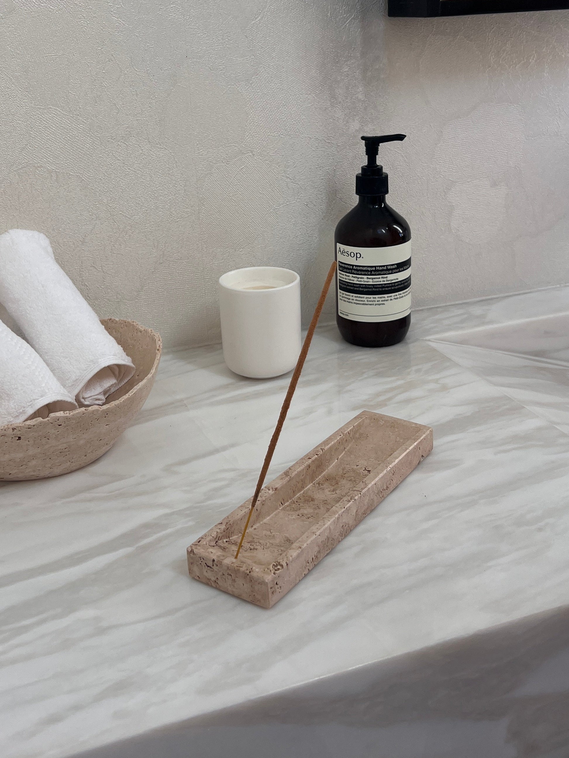 Bathroom counter with rolled towels, a bottle, and an incense stick holder.