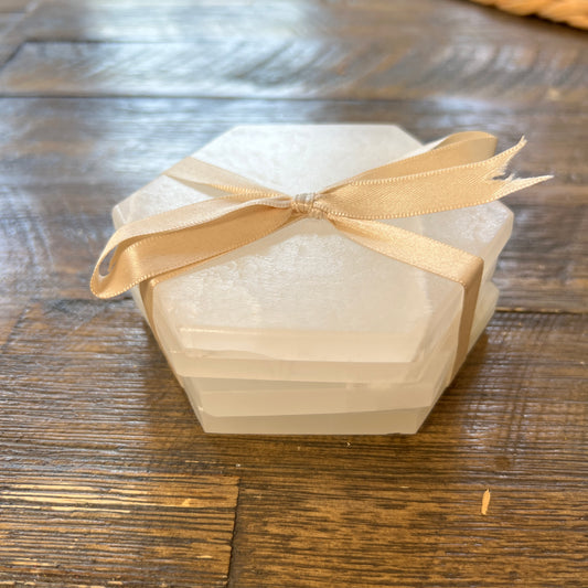 A set of white aragonite stone hexagonal coasters tied with a beige ribbon on a wooden surface