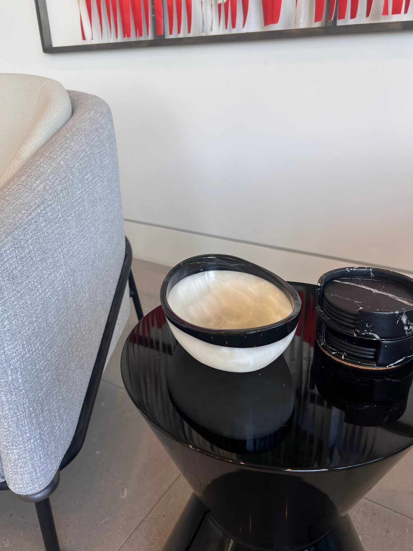 Black round table with a white bowl with black onyx rim and abstract art in the background.