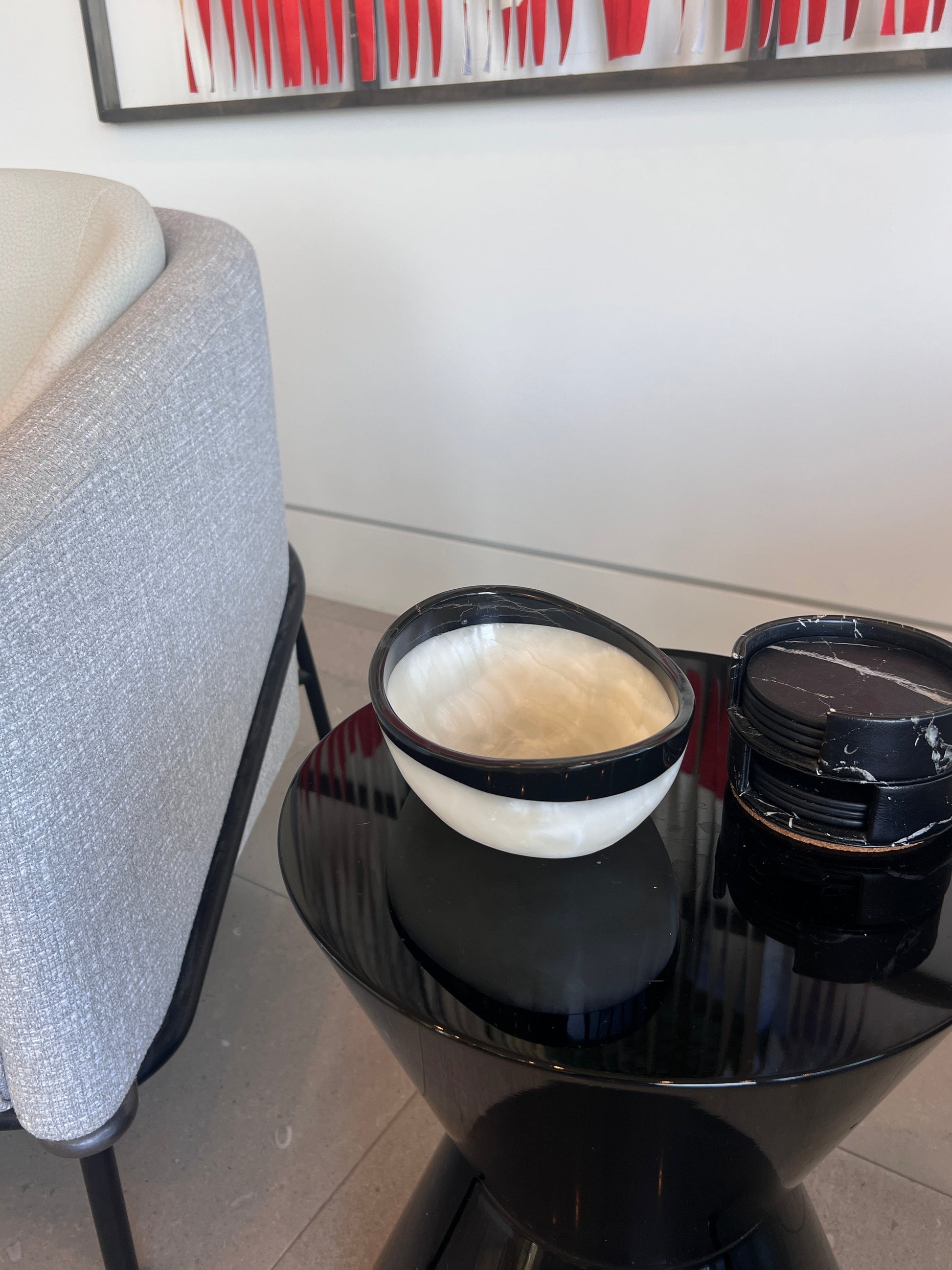 Black round table with a white bowl with black onyx rim and abstract art in the background.