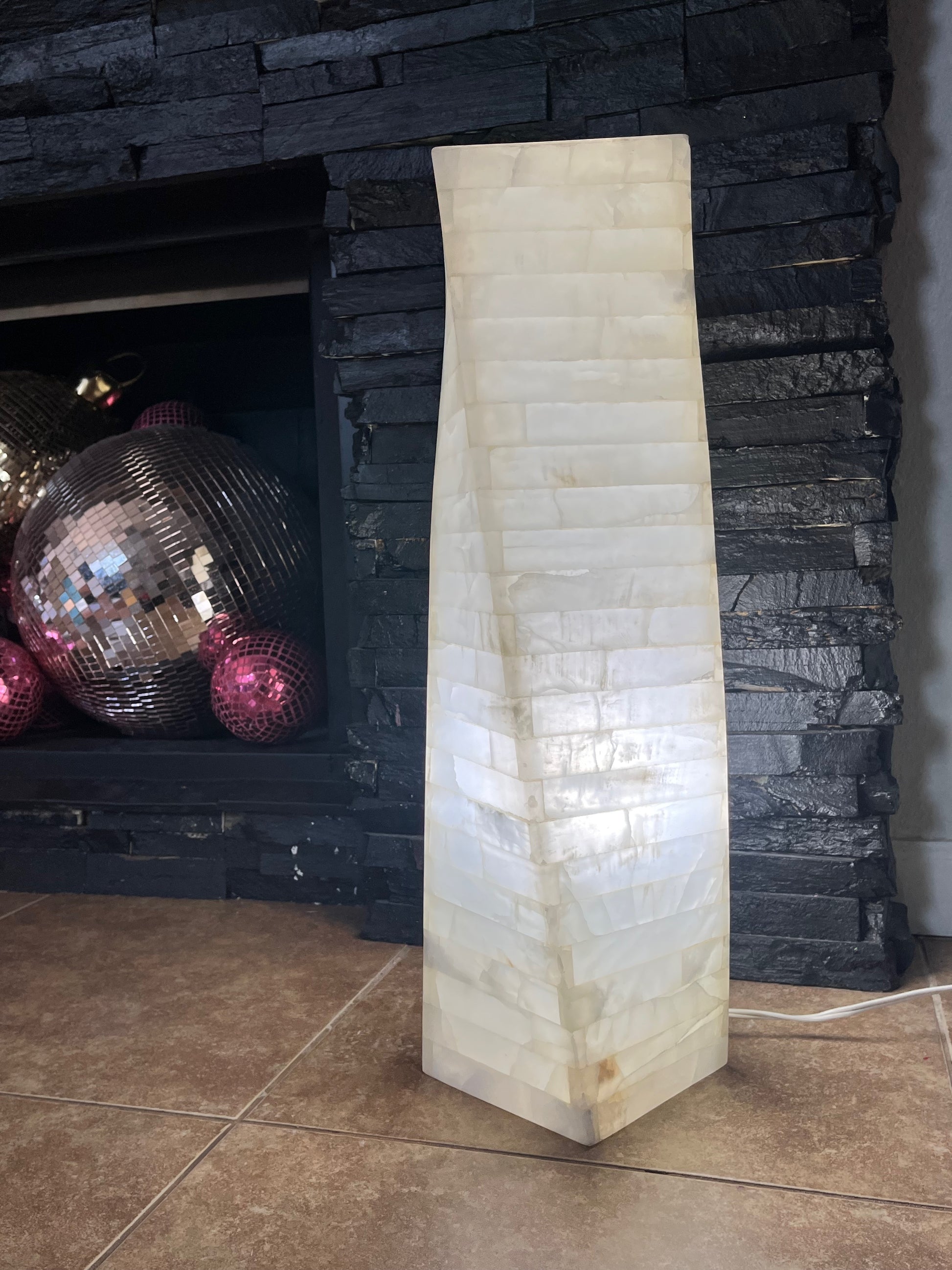 White onyx marquetry floor lamp illuminated beside dark stone fireplace
