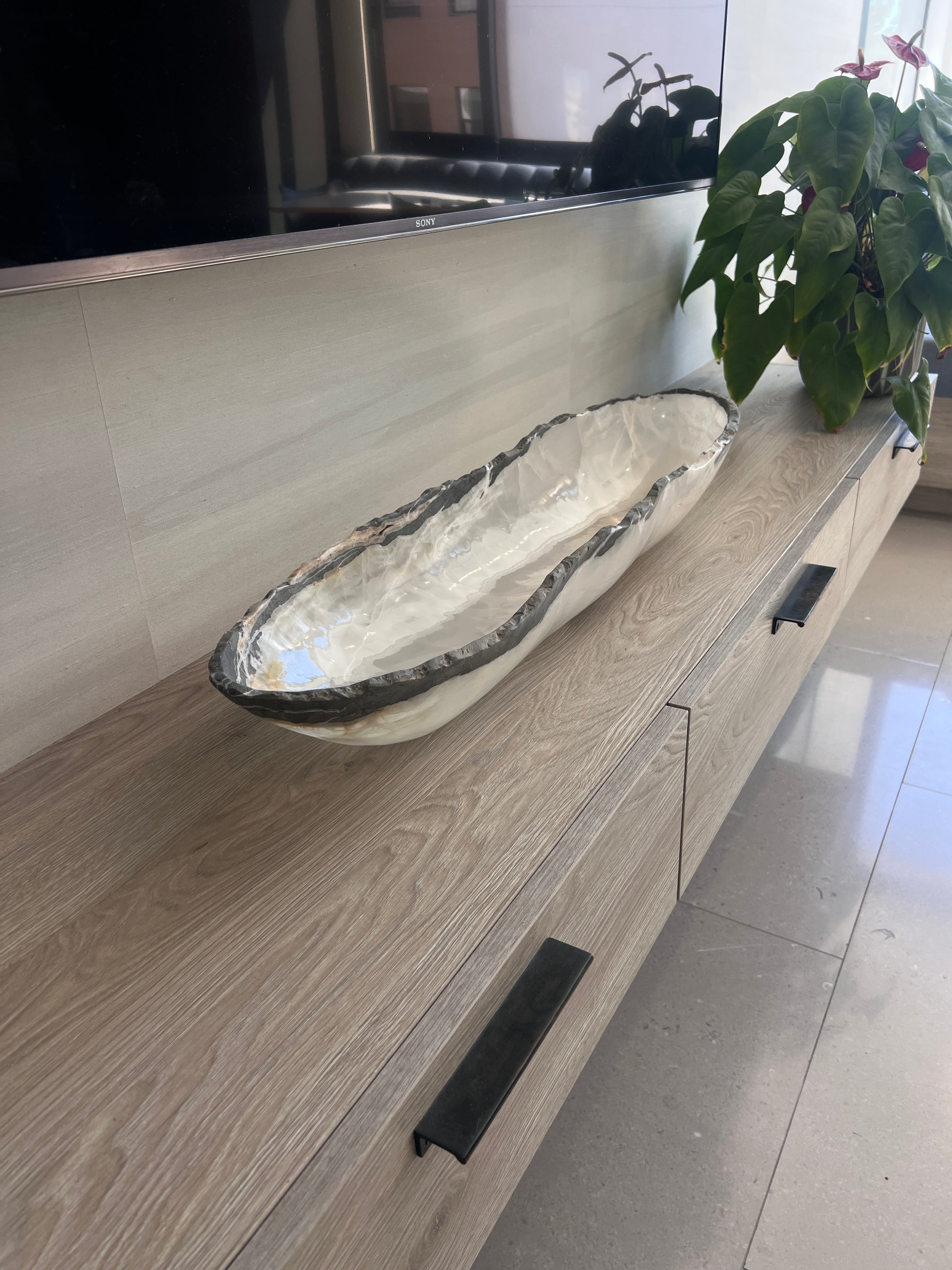 Oblong white onyx bowl on a wooden vanity with a plant in the background