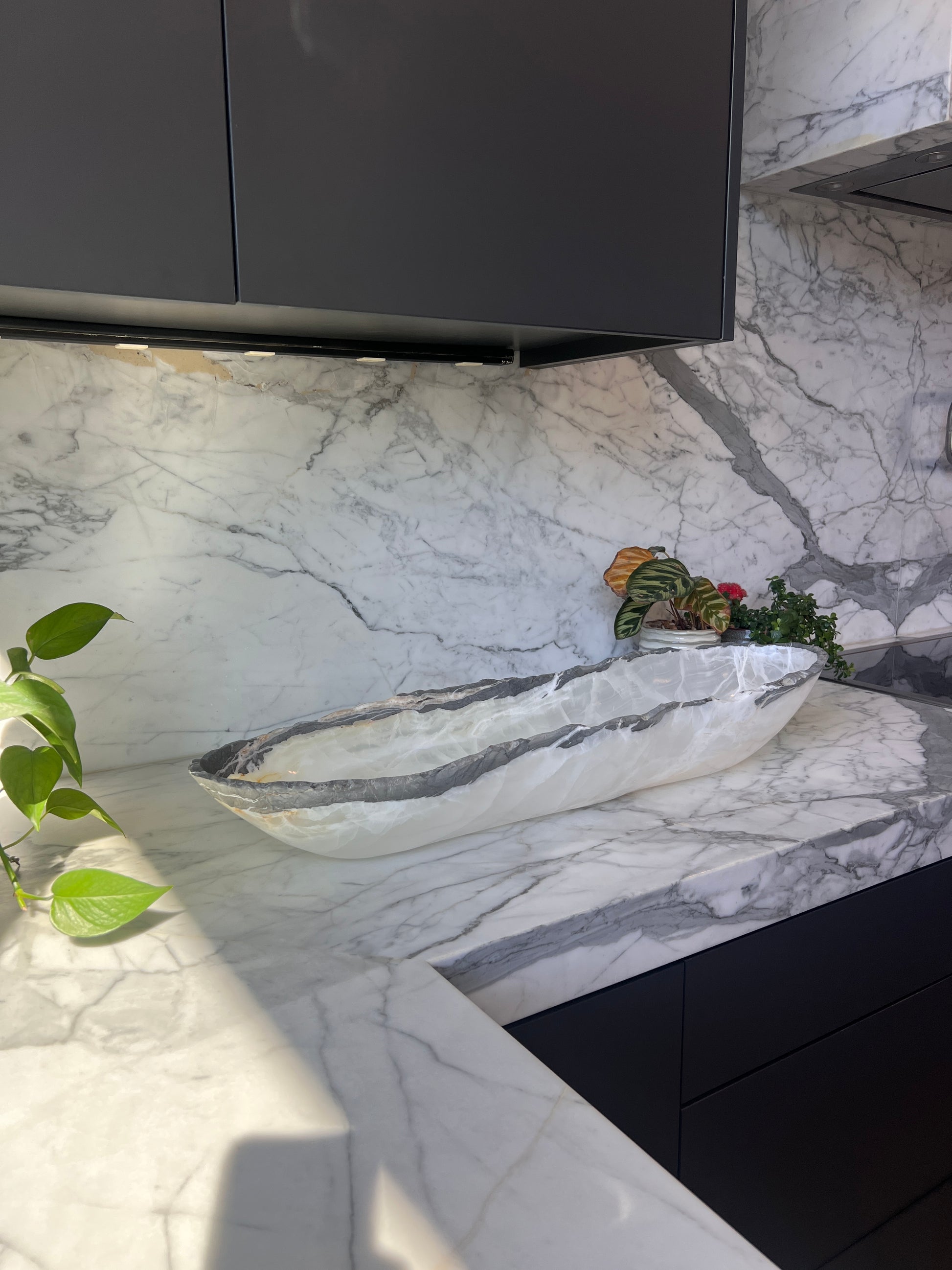 Modern kitchen with marble countertop and backsplash, featuring a white oblong bowl with grey rim.