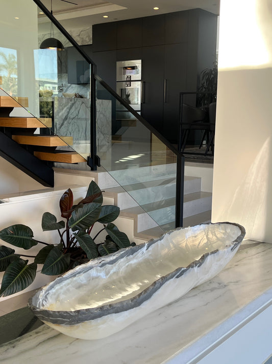Modern interior with a decorative stone bowl on a marble surface, glass staircase, and plants.