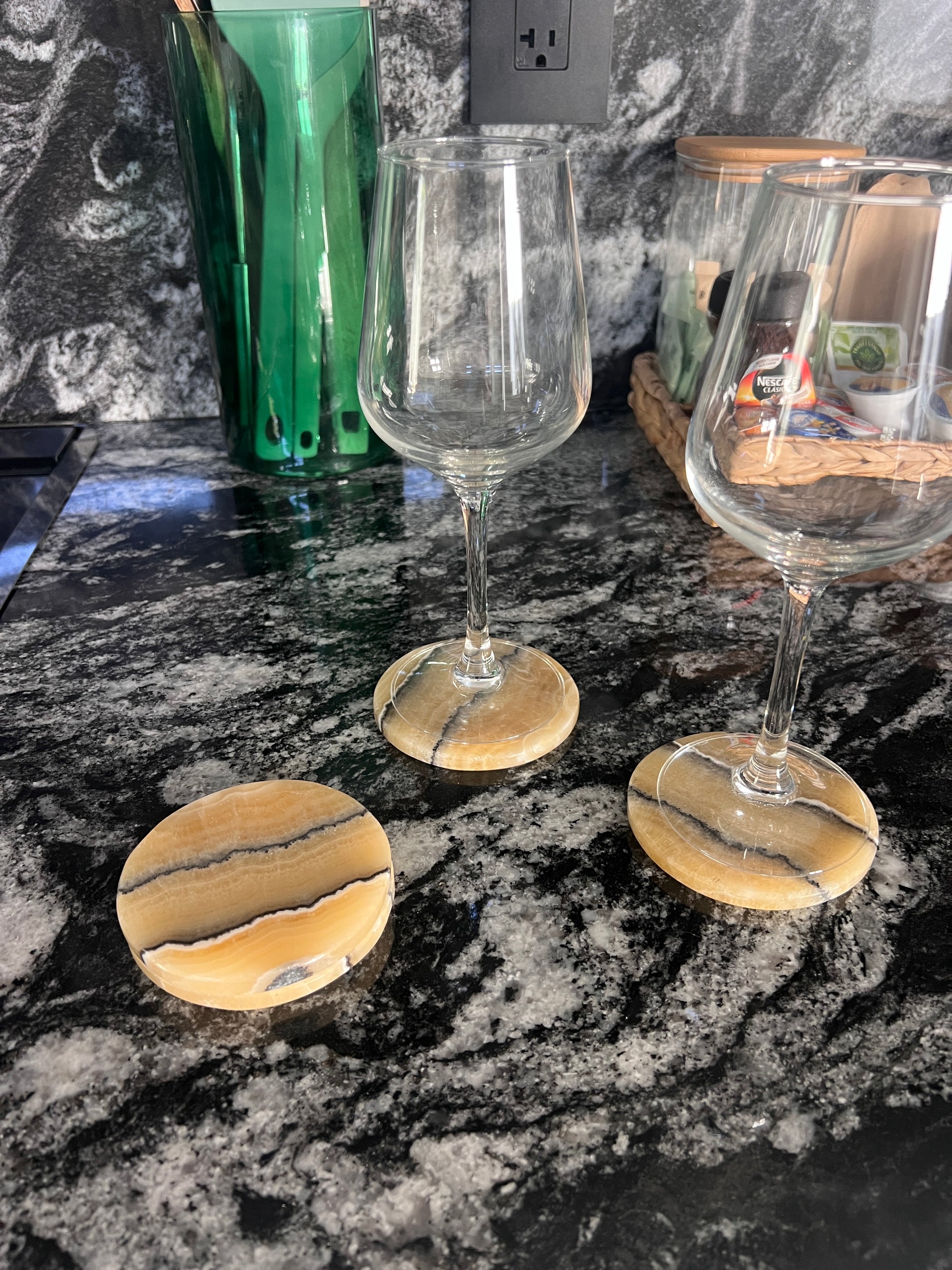 Two wine glasses on yellow coasters on a dark granite countertop.