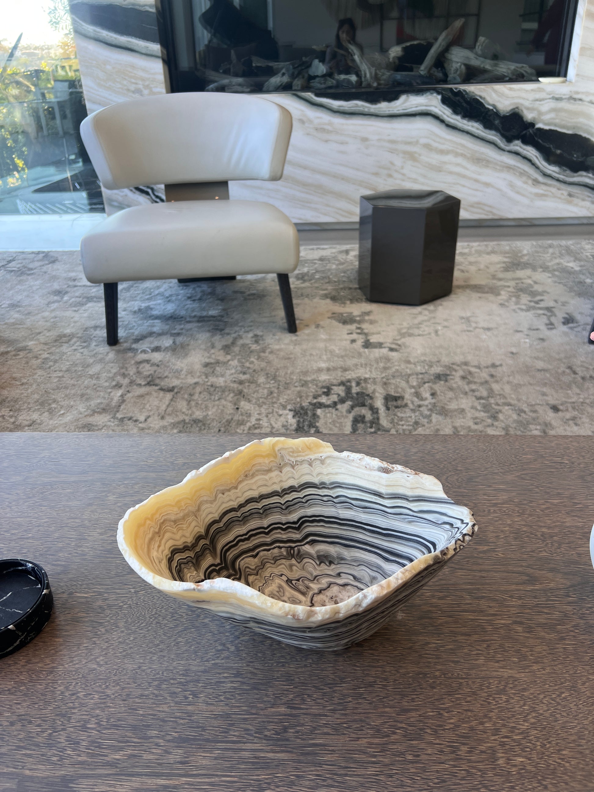 Decorative stone bowl on a wooden surface with a modern chair and fireplace in the background.