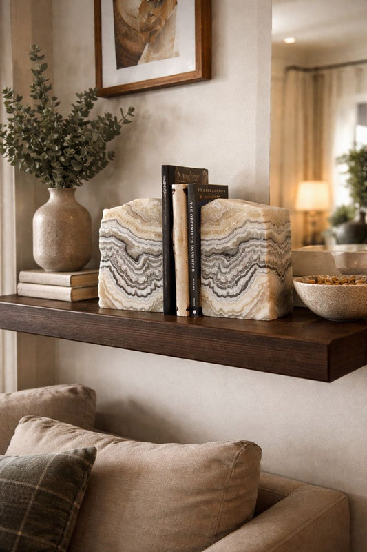 Pair of natural zebra calcite stone bookends with cream, gray, and honey banding on a decorative shelf with books and a vase on a wall above a sofa.